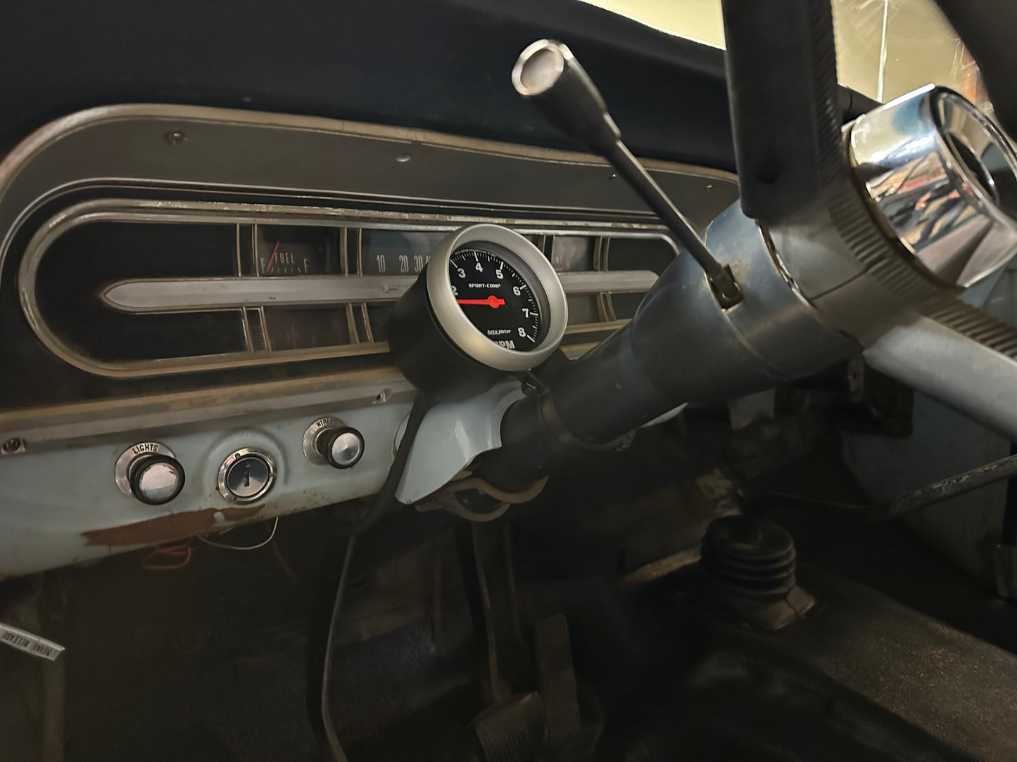 A steering column gauge mount installed in a vehicle, featuring a black gauge attached to the steering column cluster.
