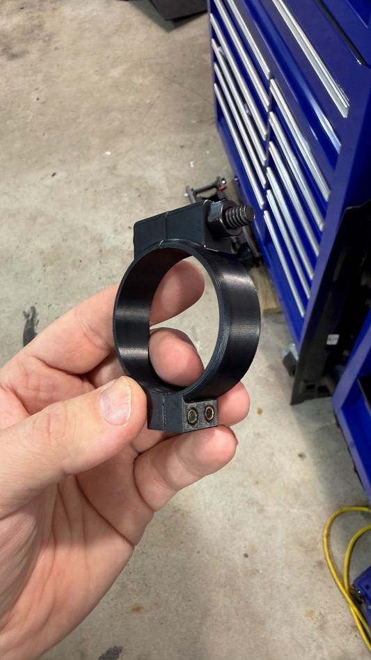 Hand holding a black metal gauge clamp component in front of a blue tool chest.